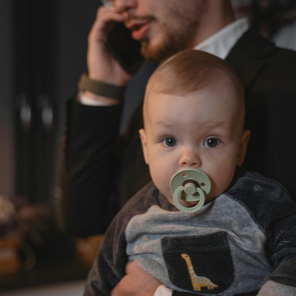 Home A father holding a baby while on a phone call, illustrating work-life balance.